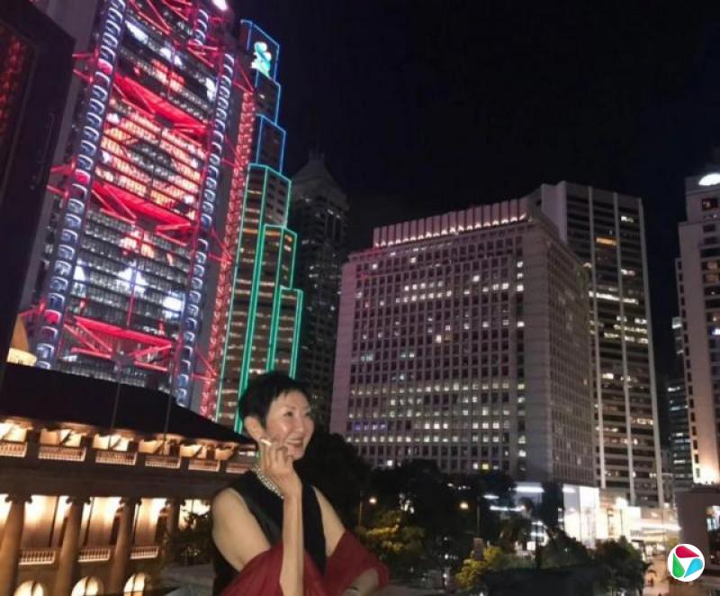 身穿晚装的施南生摄于香港会,日期不详,背景是中环夜景,从左至右分别是中国香港特区终审法院、汇丰银行香港总行、渣打银行香港总行和香港文华东方酒店