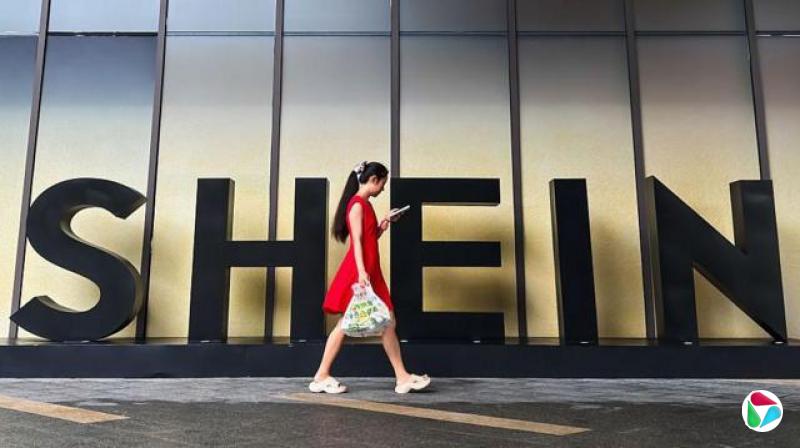 一名身穿红色连身裙的女子走过中国广州Shein办公室外的一个Shein标志时查看其智能手机。